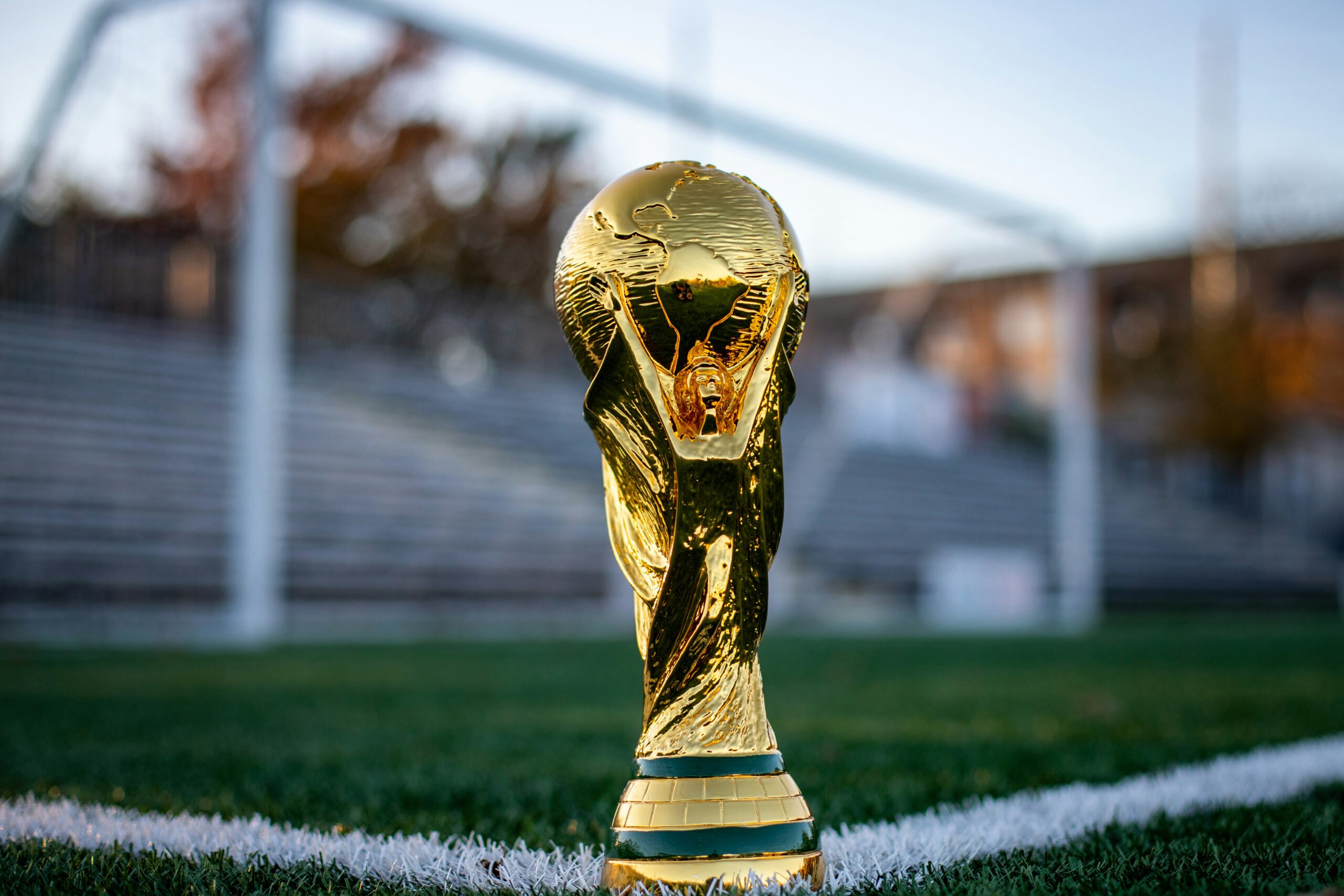 Golden World Cup trophy standing on a soccer field in front of the goal ahead of the FIFA World Cup 2026.